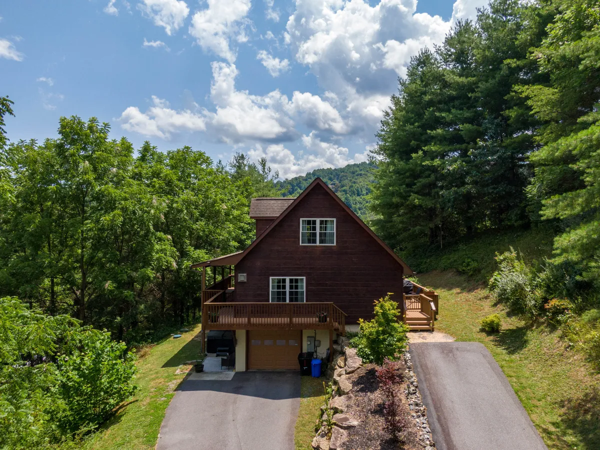 A full exterior view of the house with a charming porch, surrounded by greenery and a peaceful driveway. The setting feels tranquil and showcases the house's integration with the natural landscape.