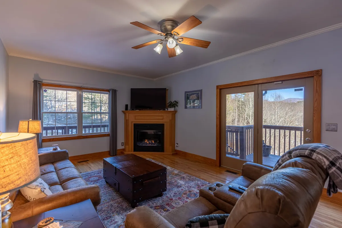 A warm and inviting seating area centered around a stone fireplace, with comfortable chairs set near a window that frames the outdoor landscape. The space is ideal for reading, relaxing, or socializing, and the fire adds to the cozy ambiance.