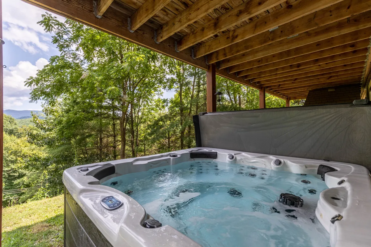 An inviting outdoor hot tub, nestled on a deck overlooking rolling hills and surrounded by lush greenery and mountain vistas. The area exudes tranquility and is perfectly set up for relaxation or family gatherings after a day of mountain exploration.