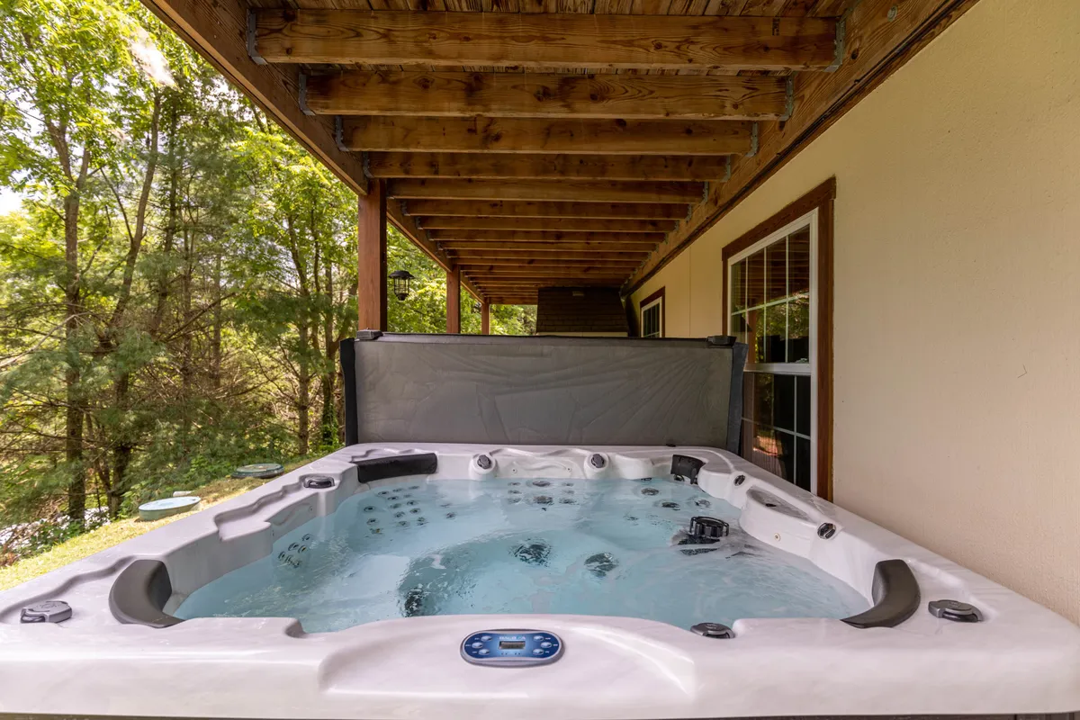 This image captures a serene outdoor hot tub set beneath wooden beams, surrounded by lush greenery. The setting is tranquil, offering an inviting spot for relaxation and recovery after a day of hiking or adventure in the mountains.