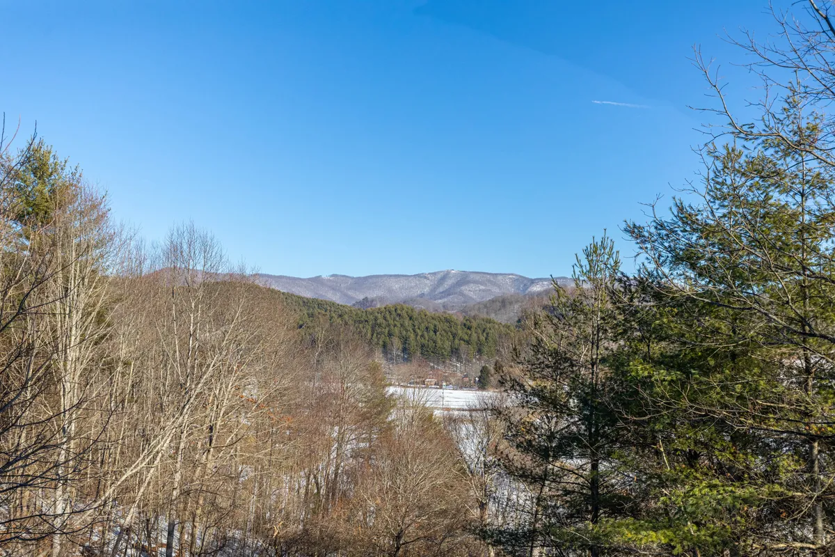 A breathtaking view over a mountain range, with a clear blue sky, dense forests, and a frozen lake visible in the distance. The scenery evokes the adventurous spirit of the nearby state parks and mountain activities mentioned in the section.