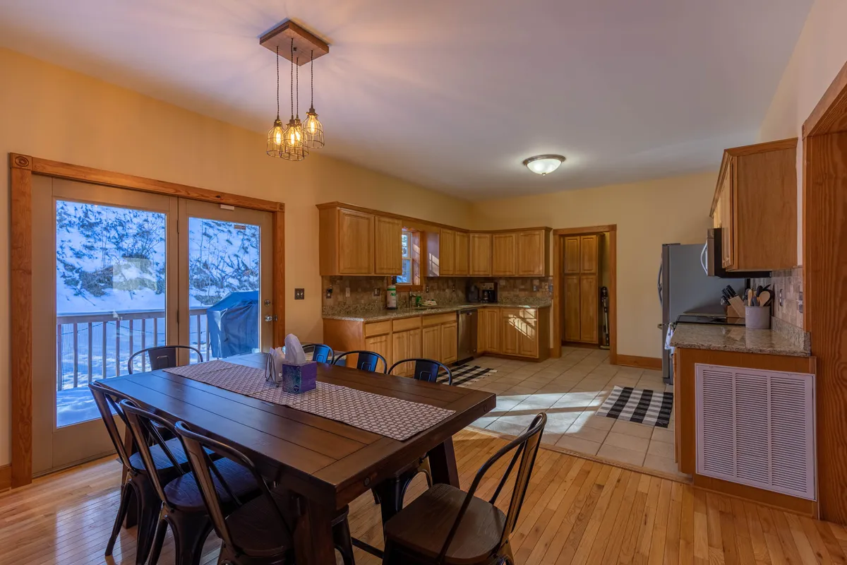 An open-plan dining area with a spacious table positioned near large windows, offering scenic views while dining. Kitchen countertops are visible, suggesting connectivity between cooking and dining spaces, and the setup encourages group meals and lively conversation.