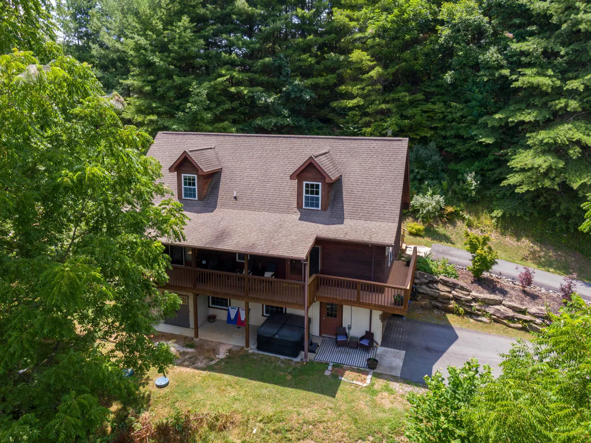 A two-story wooden house set against vibrant greenery, featuring a welcoming porch with outdoor seating. The environment is peaceful, offering a sense of privacy, comfort, and connection to nature—ideal for families returning from local excursions.