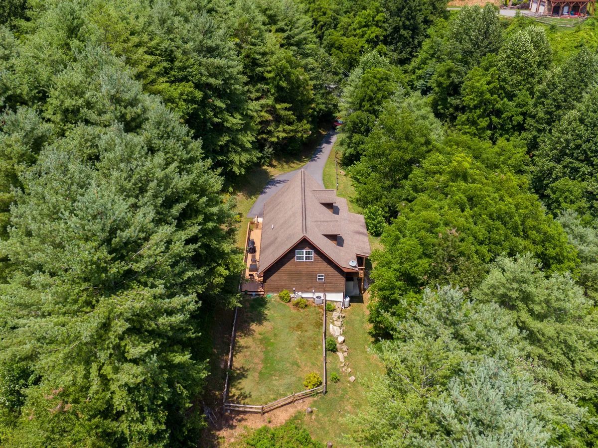 The exterior of a charming wooden house nestled among mature trees, with a welcoming driveway leading up to the entrance. The natural setting exudes peace and privacy, ideal for a mountain hideaway.