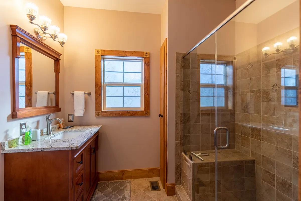 This modern bathroom includes a stylish vanity with sink, a well-lit mirror, and a spacious shower area. The calm mood and clean design make it a welcoming space for refreshing after mountain adventures.