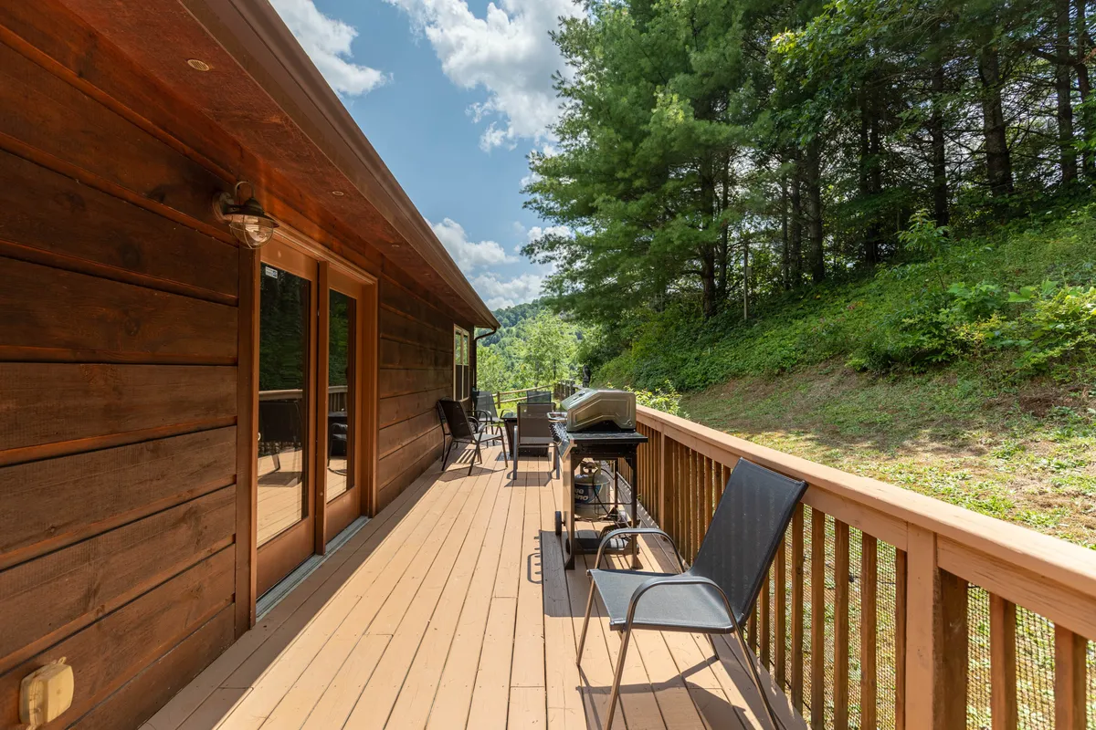 A wooden deck with outdoor chairs and a grill overlooks a lush green landscape, offering an inviting space for morning coffee, sunset barbecues, or simply relaxing and taking in the views.