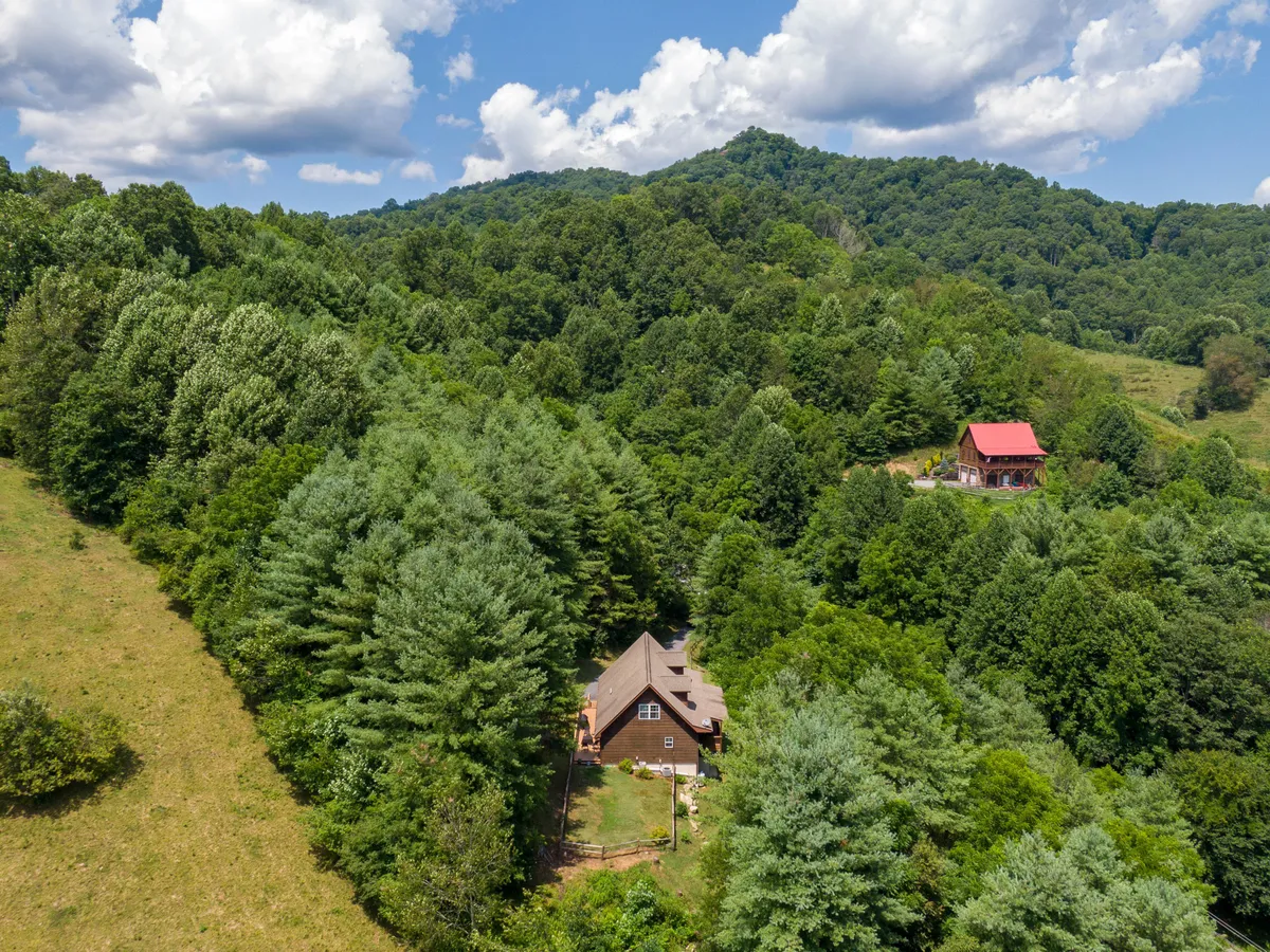 The exterior showcases the house set amidst a backdrop of trees and distant hills, evoking the sense of mountain seclusion and natural beauty. The image suggests access to hiking, birdwatching, and peaceful moments on the porch with scenic vistas.
