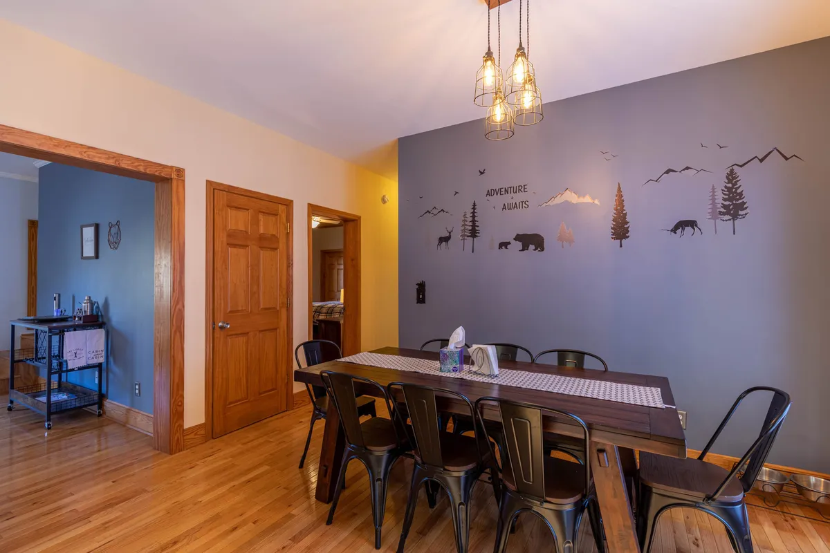 The photo displays a spacious dining area, highlighting a large dining table, artistic wall mural, and stylish lighting fixtures. The scene is set for lively gatherings, holiday meals, or casual breakfasts—suggesting versatility and comfort for communal dining.